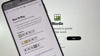 A phone held up to a PC monitor. Both are playing Wordle